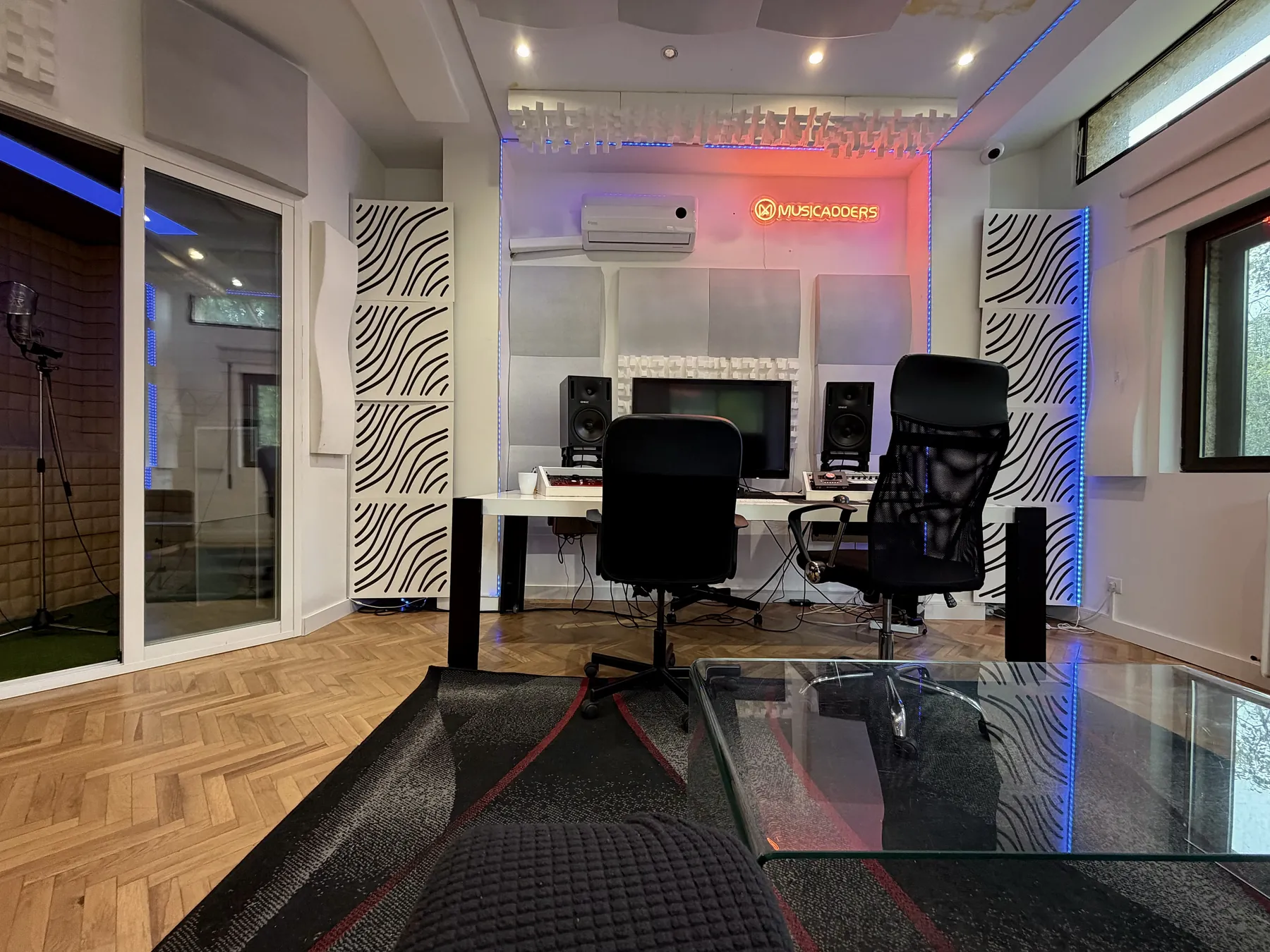 Mesa de mezcla y monitores del estudio de MusicAdders, con la cabina de grabación a la izquierda